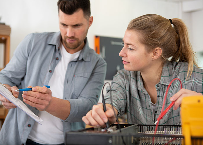 Ein Frau repariert ein Gerät, ein man hilft.